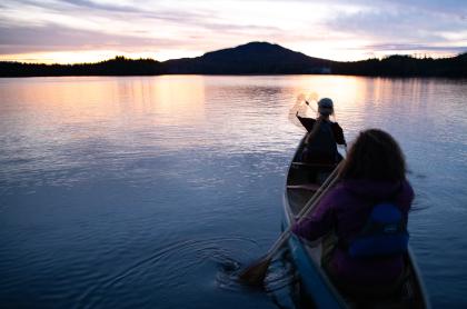 Two people canoeing towards the sunset on Lower Saranac Lake