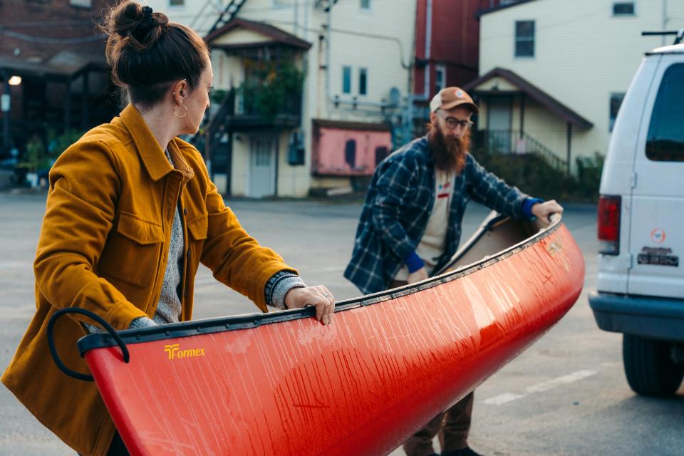 A man and woman carry a red canoe to a truck.