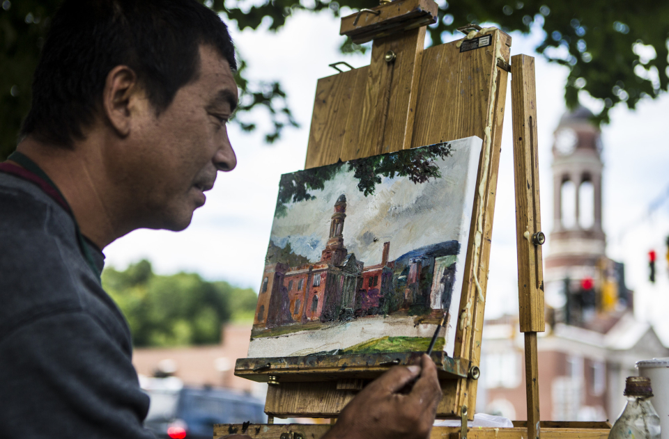 Close-up of a main painting an image of the Town Hall at an easel, with the hall in the background.