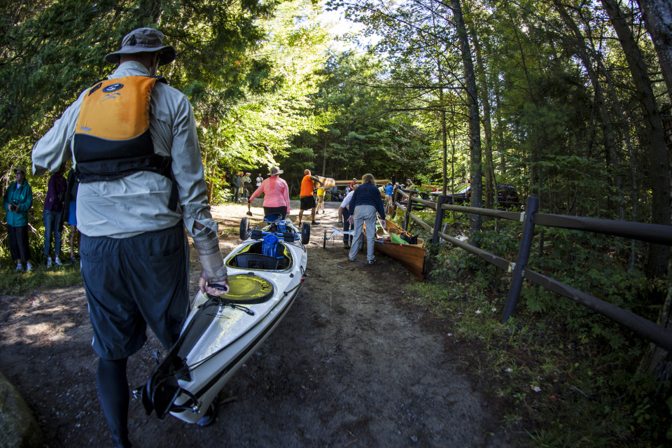 Groups of racers carrying their kayaks and canoes towards the next launching point of the Adirondack Canoe Classic