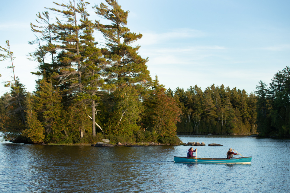 Two women paddle a blue canoe in one Saranac Lake's secluded waterways