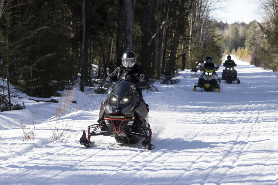 A man on a snowmobile leads a group of snowmobilers behind him on a trail.