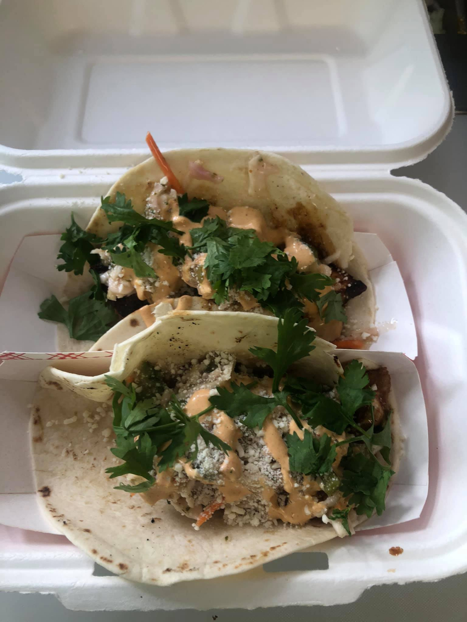 A container of two tacos loaded with fresh toppings.