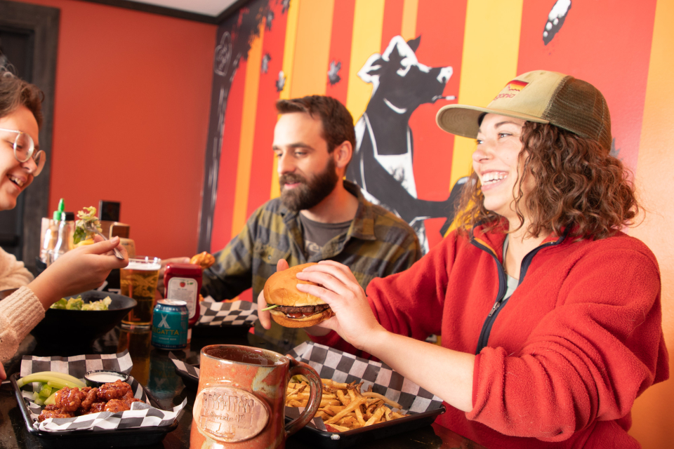 Friends enjoy a meal of wings, beer, burgers, fries, and a salad.