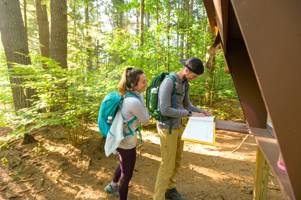 Two hikers sign in to a brown trail register