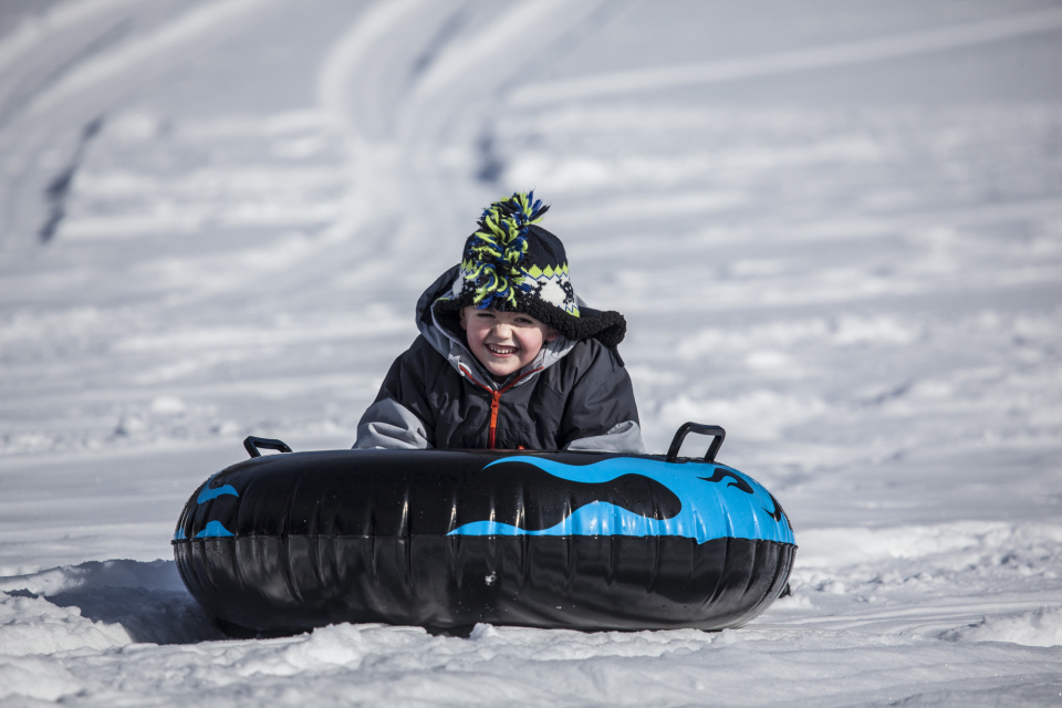 A young boy smiles as he slides down a snowy hill on a tube.