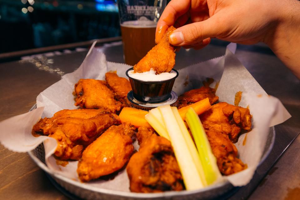 a hand dips wings into blue cheese.