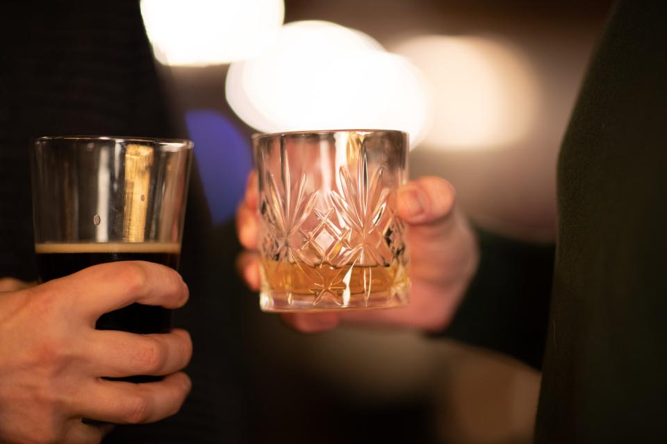 Two people hold a dark beer and a cocktail.