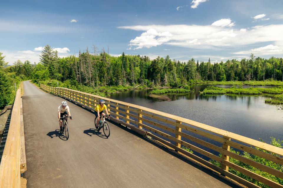 Two people ride bikes over a bridge on a marsh pond.