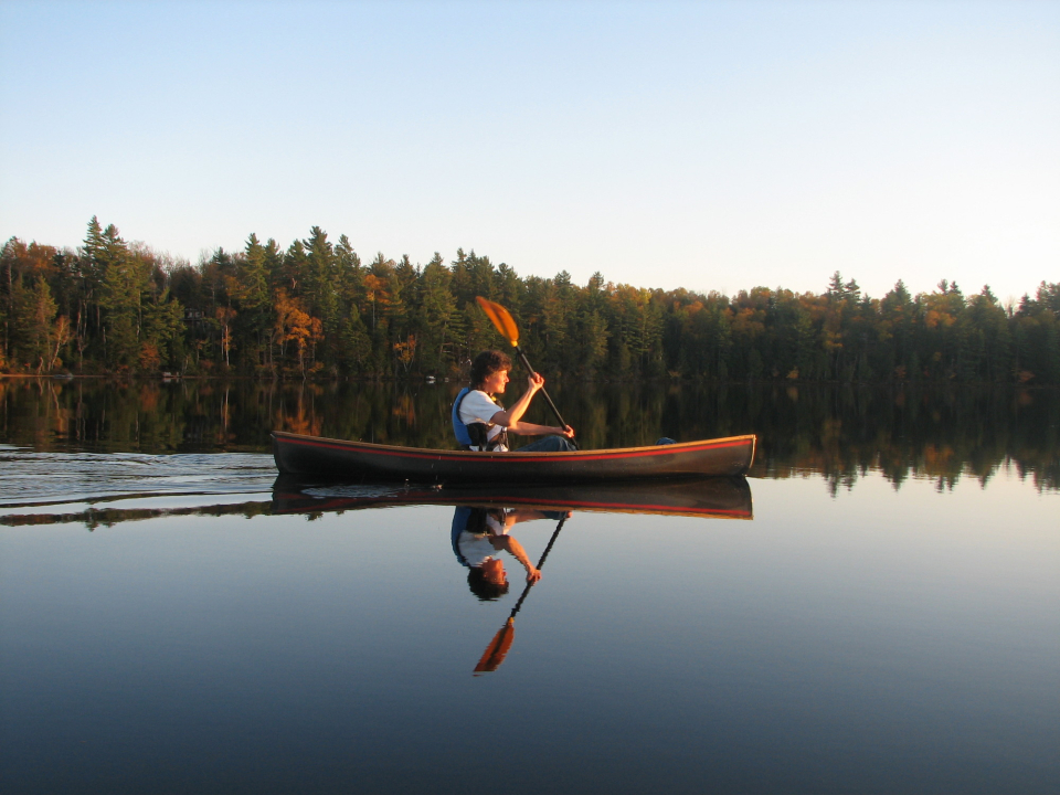 A boy paddles across a calm lake.