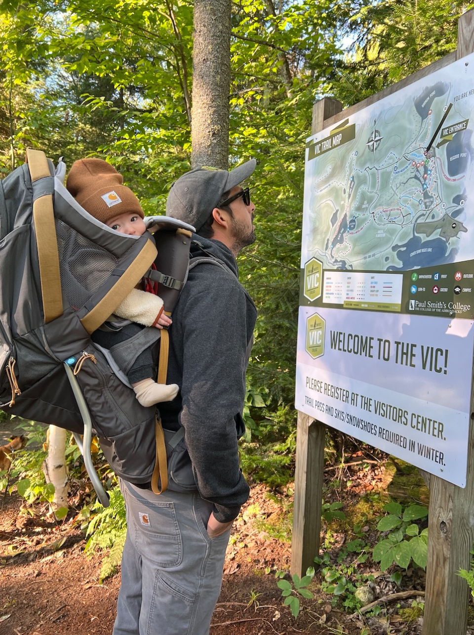 a man reads a sign with a baby strapped to his back.