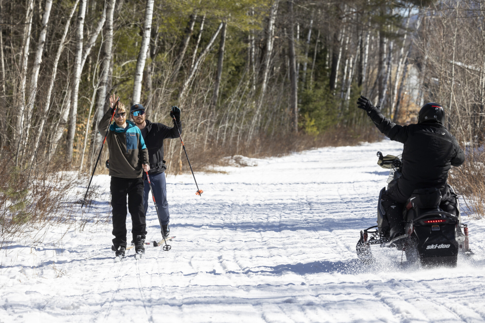 Snowmobilers and xc skiers wave to each other on a trail