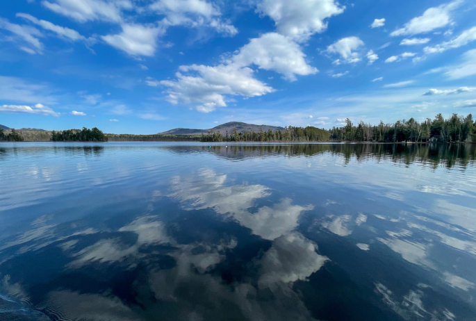 Perfectly calm waters reflect back an image of clouds and a mountain.