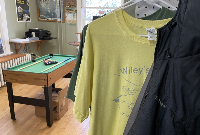 A small pool table stands beyond a tshirt display.