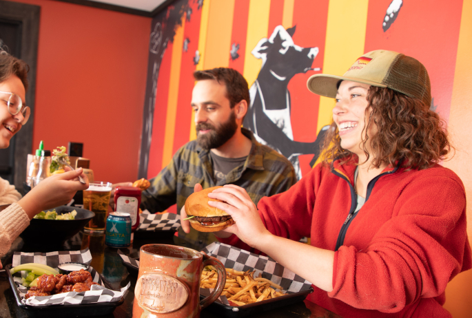 Friends enjoy a meal of wings, beer, burgers, fries, and a salad.