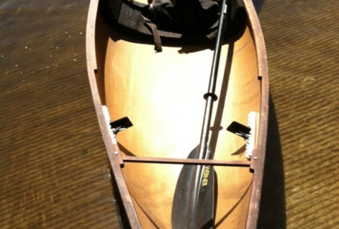 An empty brown canoe floating by the shore in shallow waters.