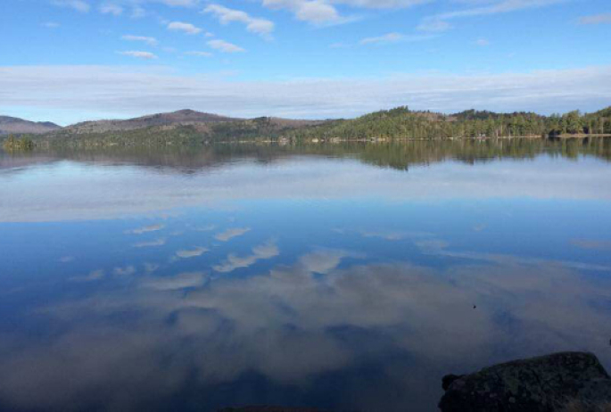 View from the shore along the Floodwood canoe route with mountains in the background and the reflection of blue skies and white clouds in the flat water