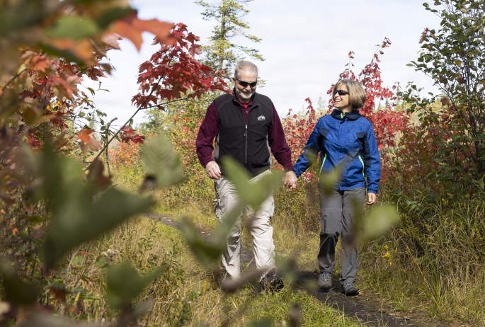 Two older hikers walk on a trail surrounded by fall foliage