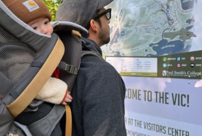 A hiker and his baby look at a map for a trail system