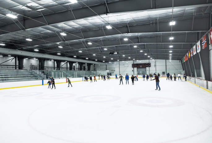 A group of people ice skate at an indoor ice skating arena.