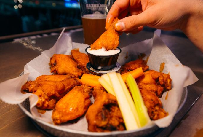 a hand dips wings into blue cheese.