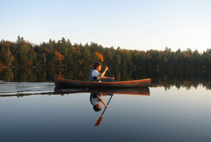 A boy paddles across a calm lake.