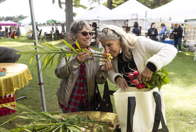 Two women inspect produce at a farmers market.