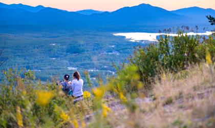 Two people look over at a view of mountains and a lake