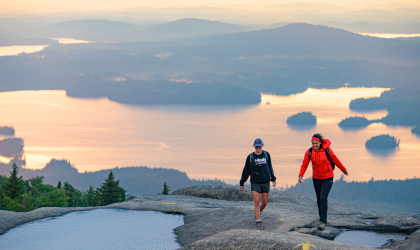 A couple people hiking Ampersand Mountain, a bare rock summit.