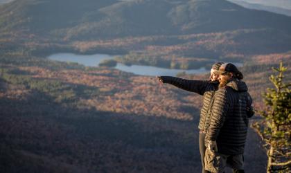 Two people enjoy a fall view from a mountain top