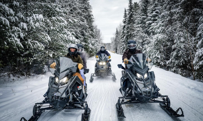 the fleet of Polaris machines riding down a freshly groomed trail lined with snow-covered pines