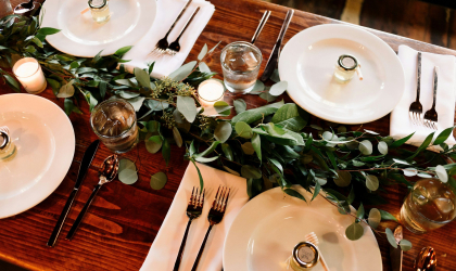 Place settings surrounded with greenery in preparation of a lovely wedding reception.